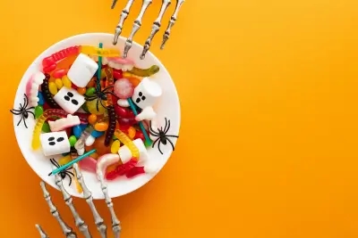 Two skeleton hands over a bowl of creepy candy and Halloween sweets.
